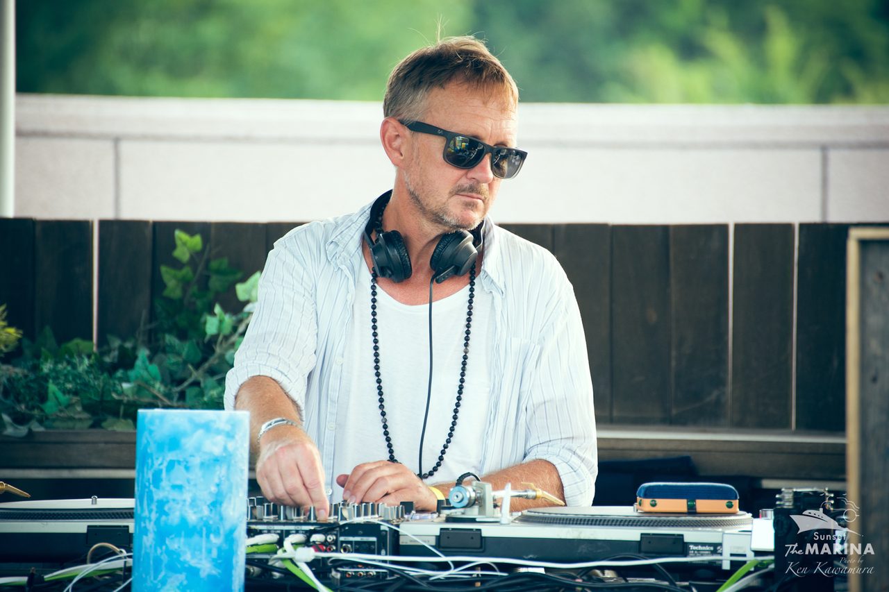 Chris Coco behind the decks in headphones at an open-air booth