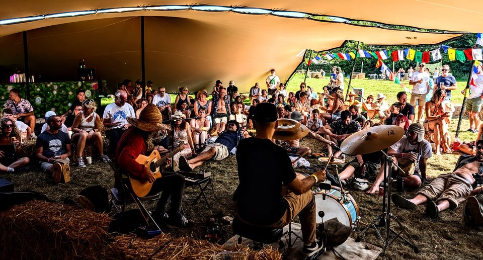 A packed afternoon crowd sitting on the grass inside The Chill Out Tent at We Are Love 2024, with a guitarist playing